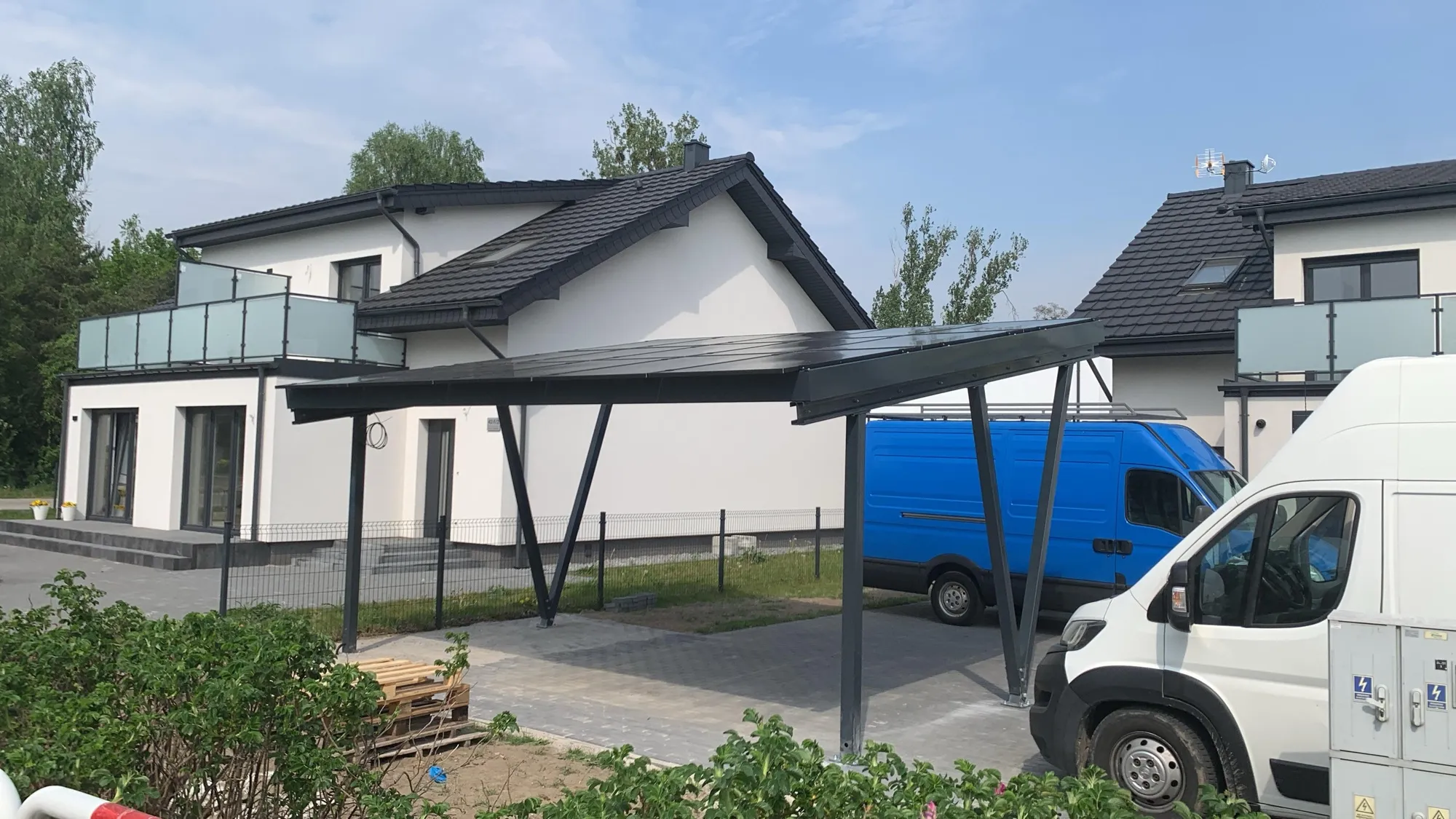 Carport z modułami fotowoltaicznymi w zadaszeniu, obok domu jednorodzinnego